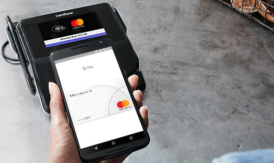 Hand placing phone on card reader to pay using Google Pay