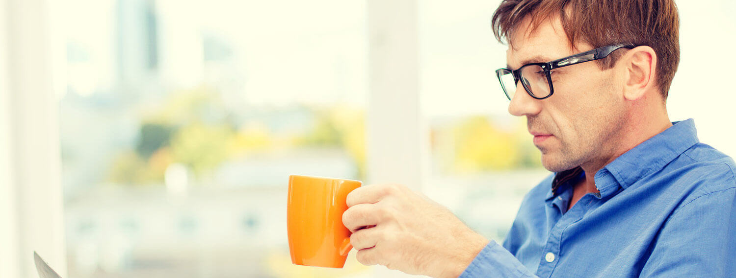 man drinks coffee as he uses his computer