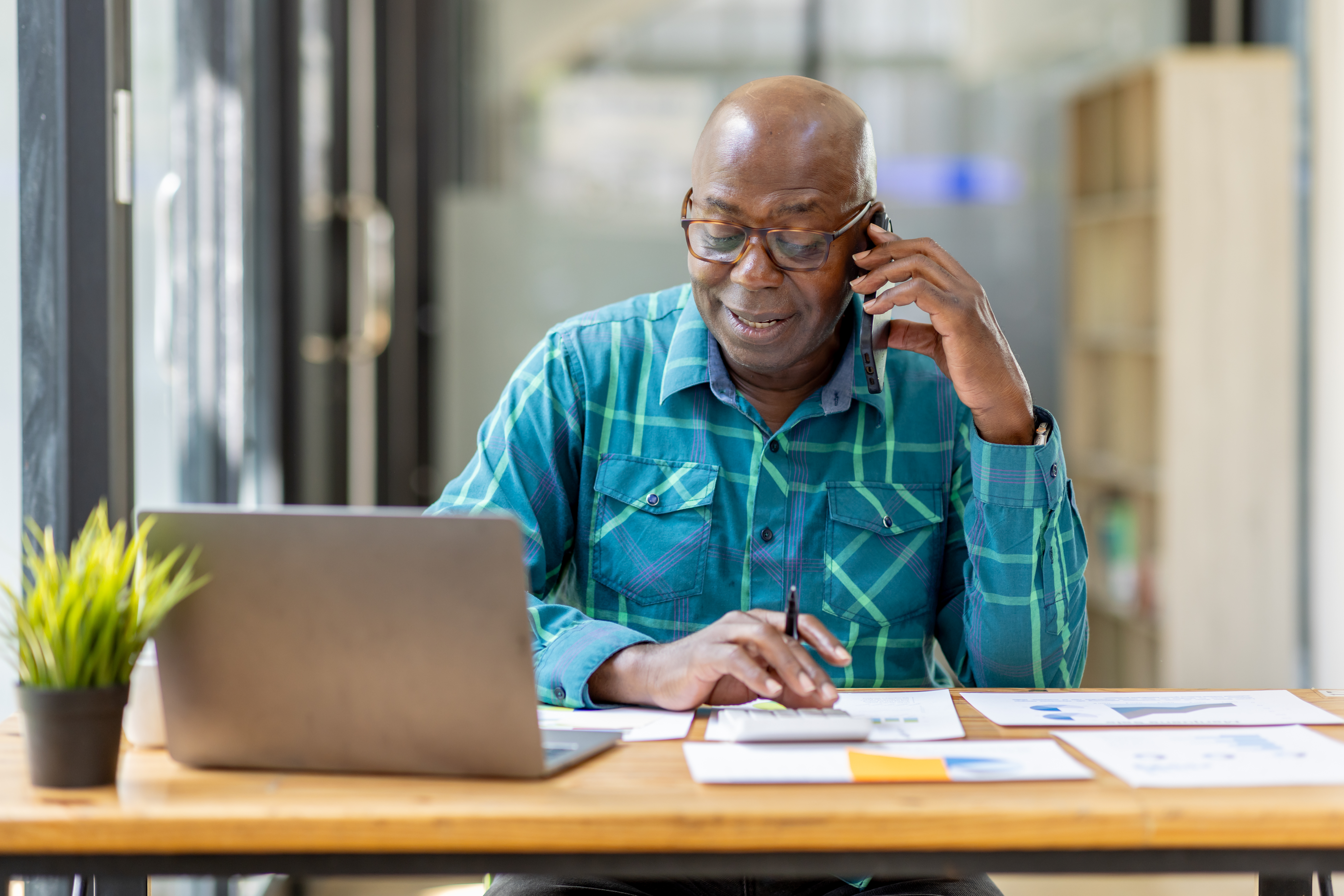Portrait of Senior African man sitting on laptop at the home office and having a phone conversation