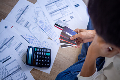 Person looking down at a calculator and credit card bills, holding credit cards in their hand