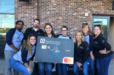 FNBT team surrounding a poster of the First National Bank and Trust Sky Carp debit card for a group photo