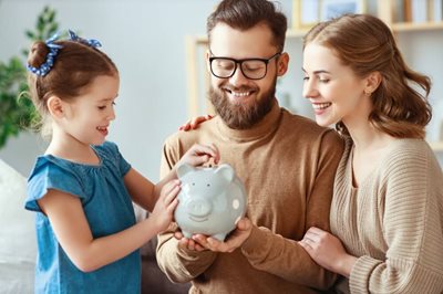 young couple and daughter putting money in piggy bank