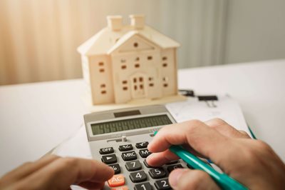 Person hitting buttons on a calculator in front of a small wooden model of a home