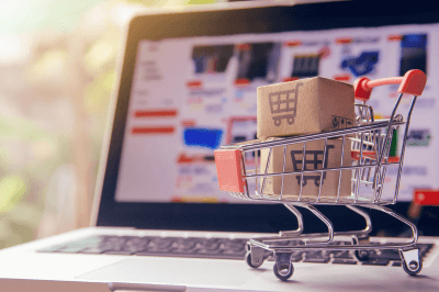 Mini shopping cart with boxes in it while on top of a laptop with a ecommerce site open