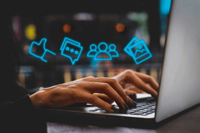 hands typing on a laptop while digital media icons float above the hands