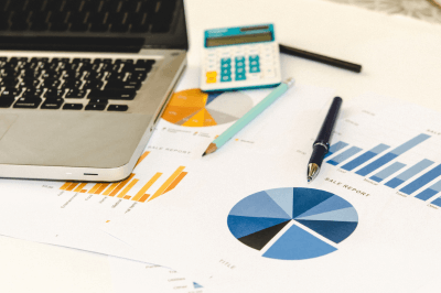 Laptop next to papers with pie charts and graphs