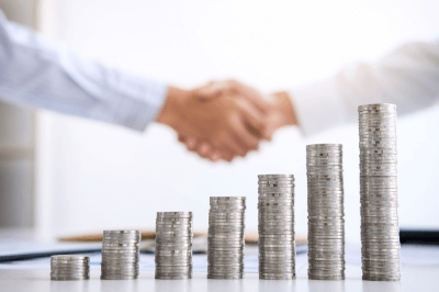 Two men shaking hands in the background of a coins signifying an investment