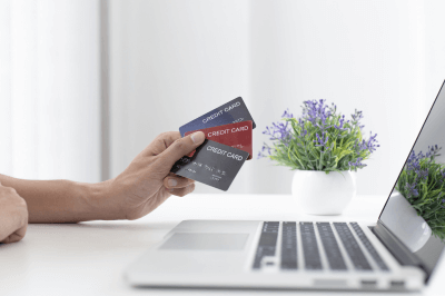 someone holding three credit cards in front of a laptop