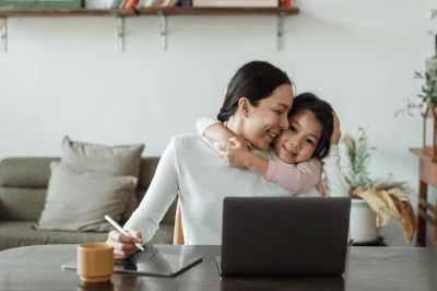 Daughter hugging her mom while she works from home on her laptop