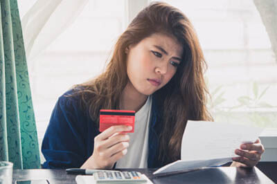 Woman holding her credit card and looking at her statement with an unhappy expression on her face