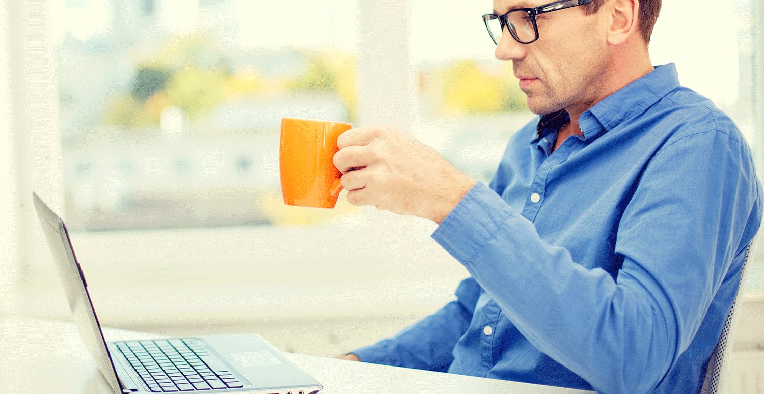 Man drinks coffee while he uses his laptop