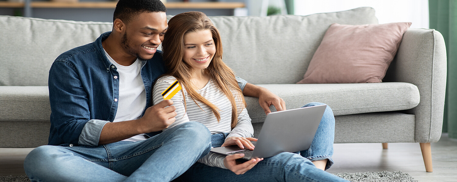 Couple online shopping on laptop sitting in front of couch