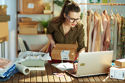 Female business owner of as clothing shop holding a package and looking at her laptop