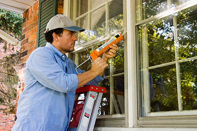 Man on a later caulking windows