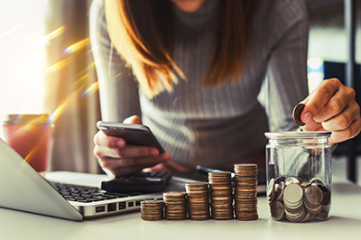 Woman putting coins in a jar next to stacks of coins