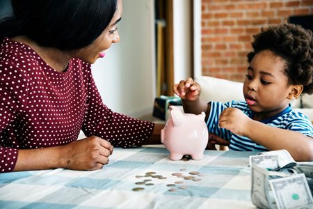 woman teaching kid about money piggy bank